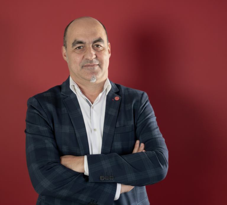 tu gestor SEAG Hombre de mediana edad con chaqueta a cuadros y brazos cruzados, fondo rojo.