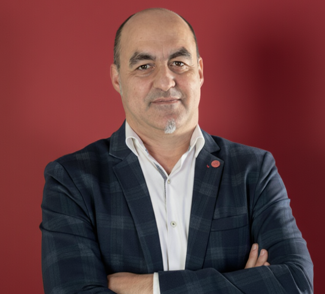 tu gestor SEAG para Barcelona y Santa Coloma de Gramanet Hombre con chaqueta de cuadros y camisa blanca, sonriendo, frente a fondo rojo.