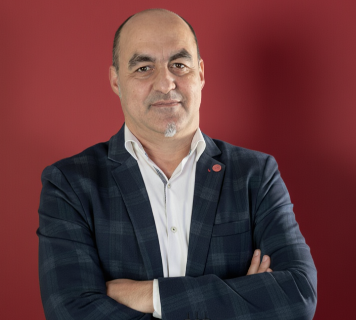 gestor Hombre de mediana edad con chaqueta a cuadros y fondo rojo, brazos cruzados.